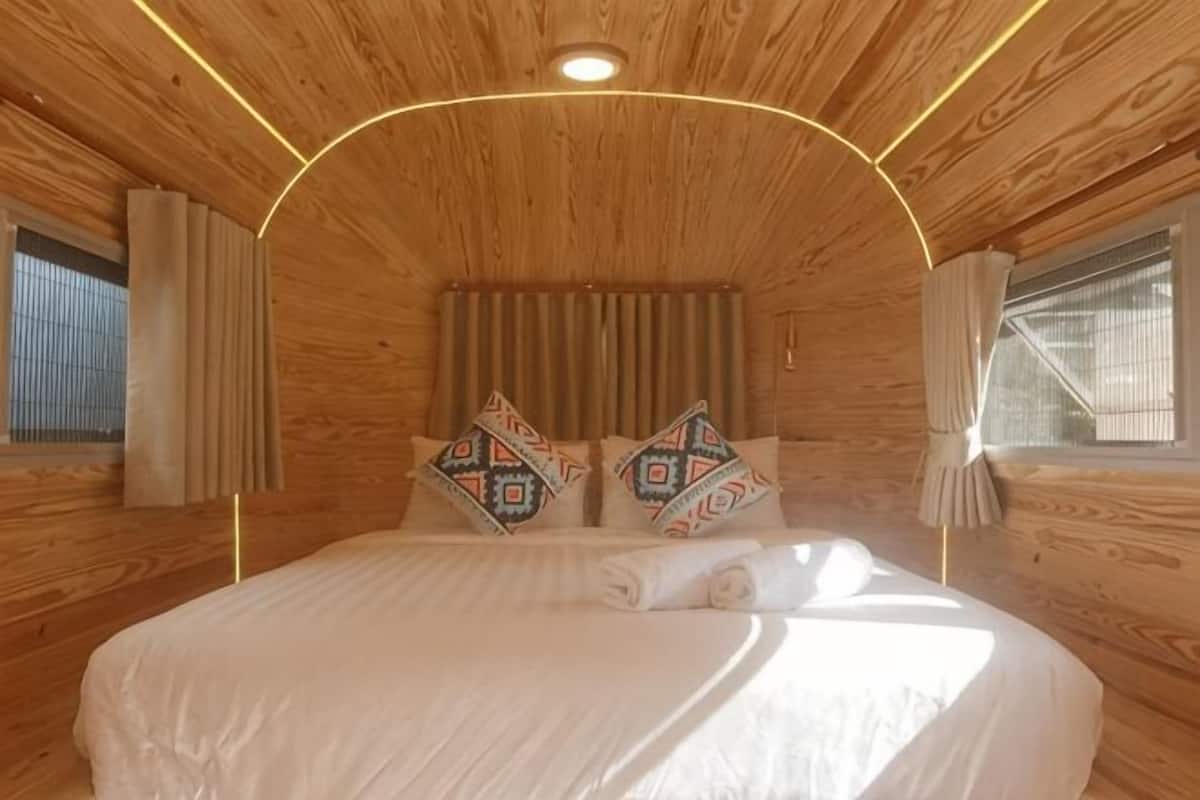 Ein Schlafzimmer in einer Holzhütte mit Bett, Kissen, Vorhängen und einem Fenster.