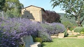 A stone building with a sloped roof, surrounded by a well-maintained garden with lavender bushes. - Villa in Cortona with 3 bedrooms sleeps 8 (Cortona)