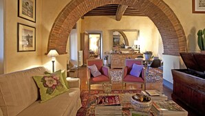 A cozy living room with a brick archway, a sofa with floral pillows, a coffee table with magazines, and a dining area with chairs and a table. - Villa in Cortona with 3 bedrooms sleeps 8 (Cortona)