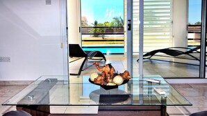 Un interior moderno con una mesa de vidrio que exhibe una decoración, una silla negra y vistas al exterior a través de una puerta corredera.