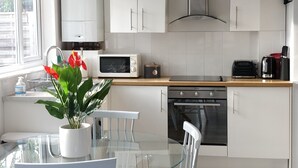 A modern kitchen with white cabinets, a stainless steel range hood, a microwave, and a coffee maker. - Sunny detached bungalow with private courtyard (Bishop's Stortford)