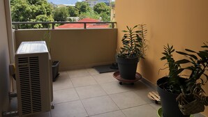 A balcony with a potted plant, a small table, and an air conditioning unit. - Appartluxe (Papeete)