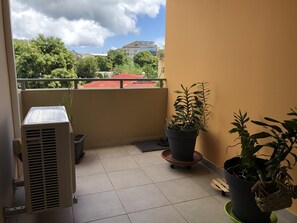 A balcony with a potted plant, a small table, and an air conditioning unit. - Appartluxe (Papeete)