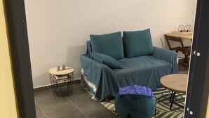 A living room with a teal sofa, a small round table, and a coffee table. There is a painting on the wall and a patterned rug on the floor. - Appartluxe (Papeete)