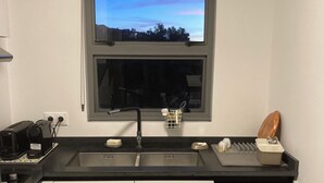 A modern kitchen with a window, a dishwasher, and a countertop with various appliances. - Appartluxe (Papeete)