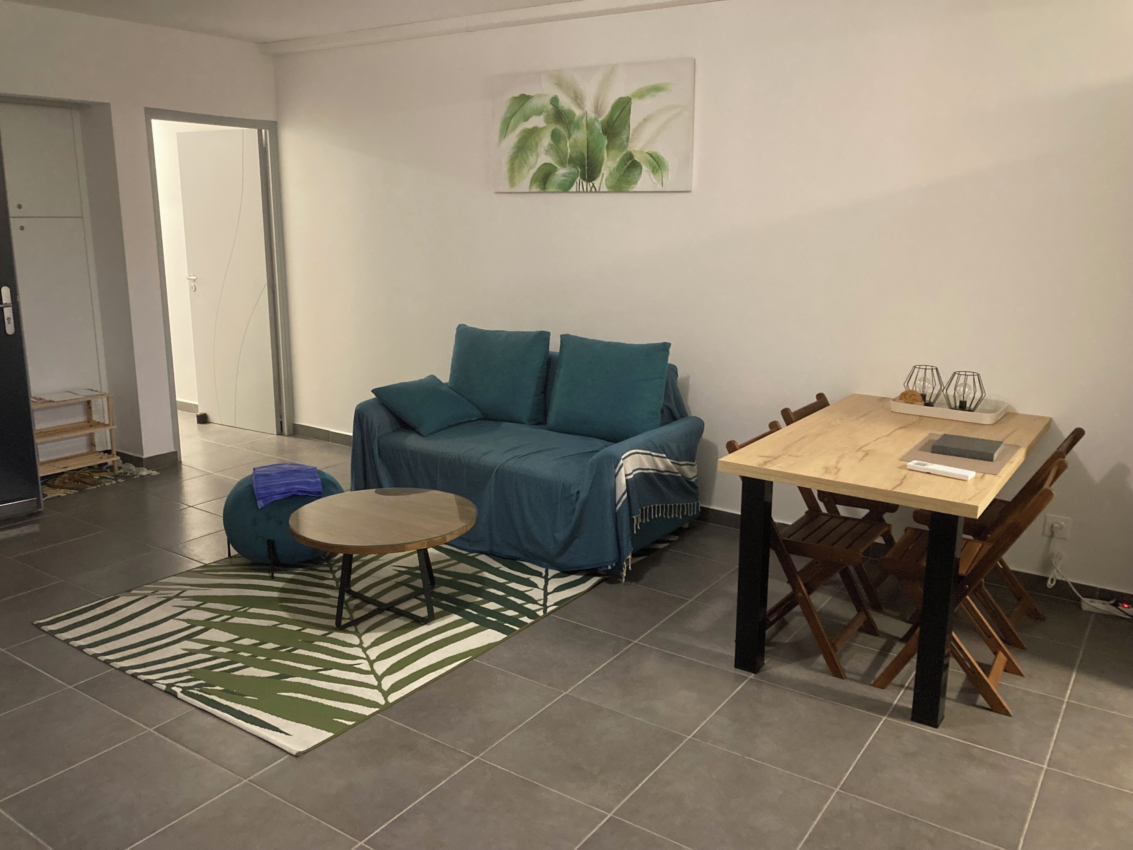 A living room with a sofa, a small round table, a dining table with chairs, a patterned rug, and a painting on the wall.