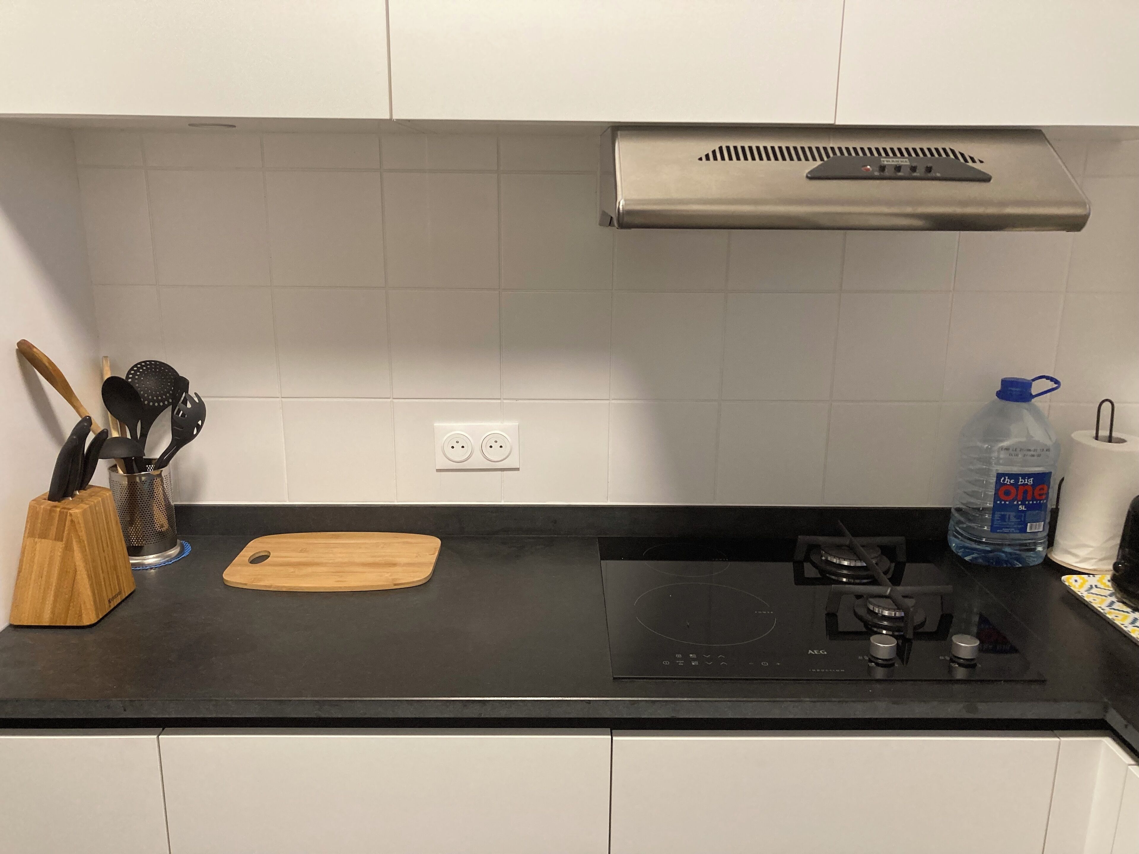 A kitchen with a black countertop, a wooden cutting board, a water dispenser, and a gas stove.