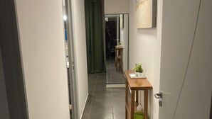 A hallway with a tiled floor, a wooden table with a plant, and a painting on the wall. - Appartluxe (Papeete)