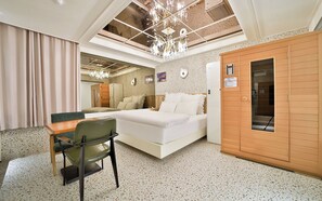 Habitación de hotel con cama, escritorio, silla, armario de madera y techo con candelabro.
