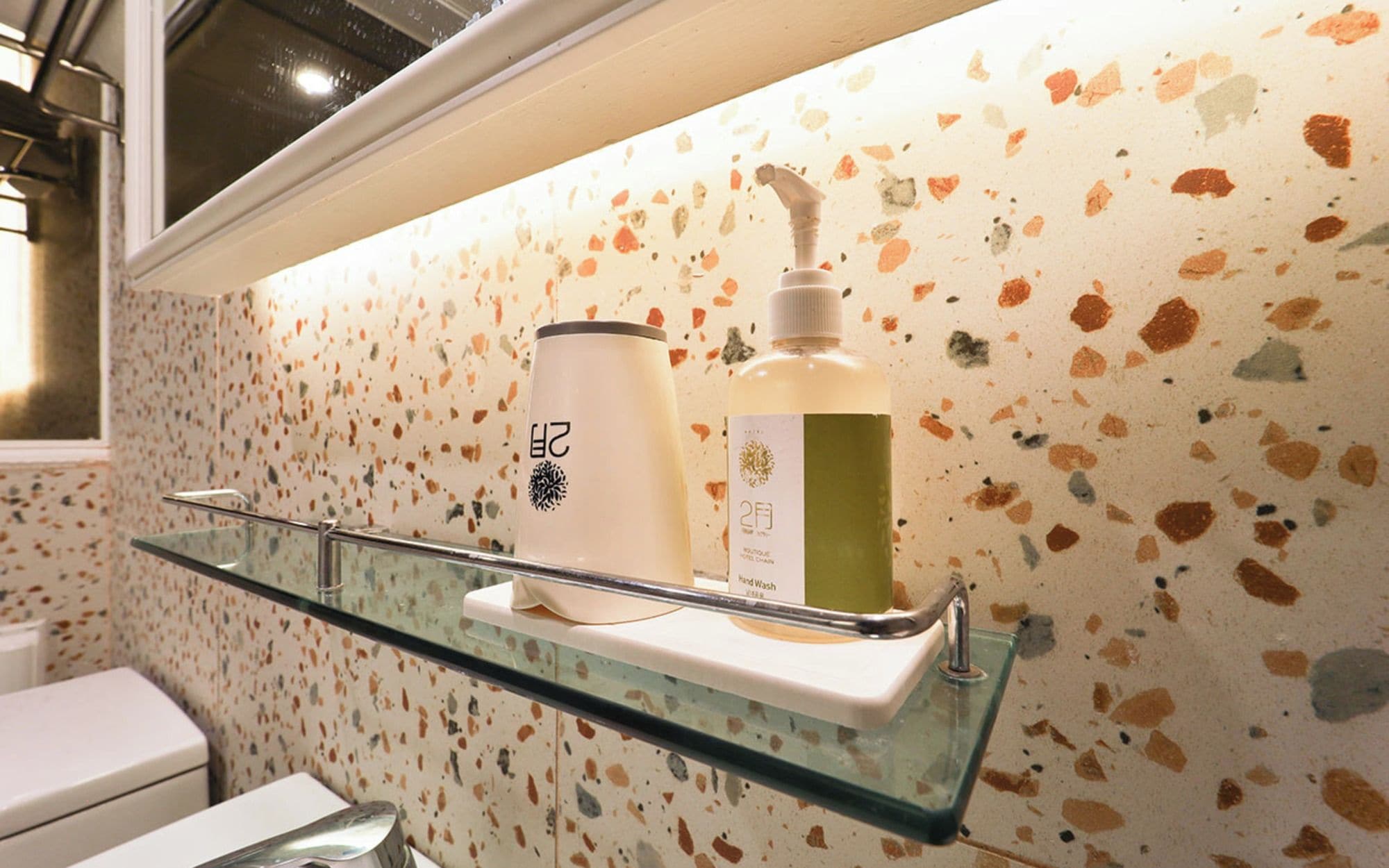 Un baño con repisa de vidrio que sostiene una botella de jabón de manos y un recipiente.