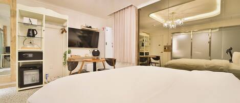 A modern hotel room with a large bed, a television, a desk with a chair, a wardrobe, and a chandelier.