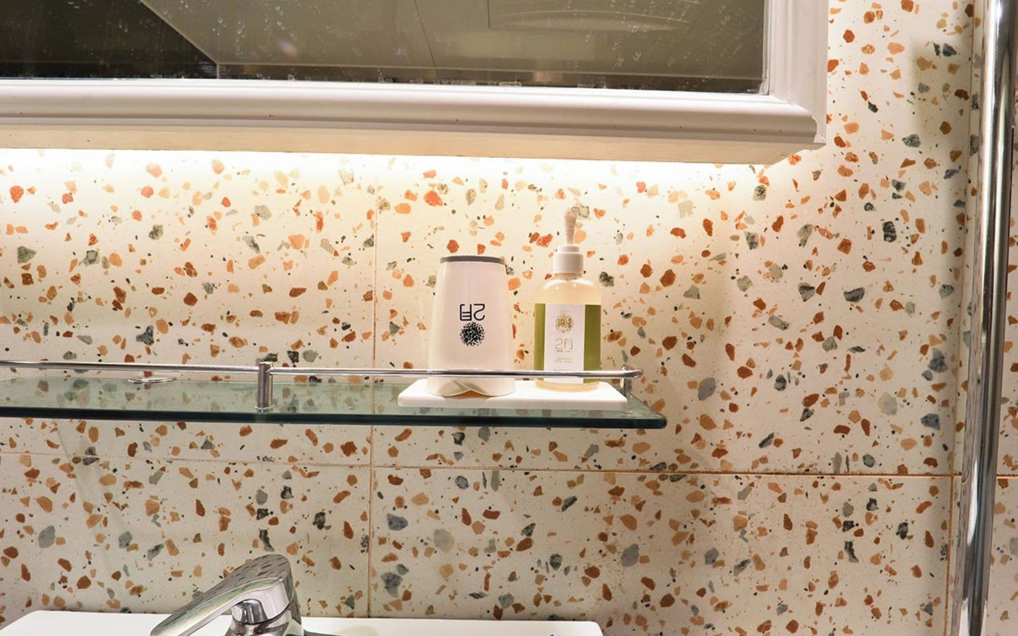 A bathroom with a glass shelf holding a white bottle and a pump bottle.