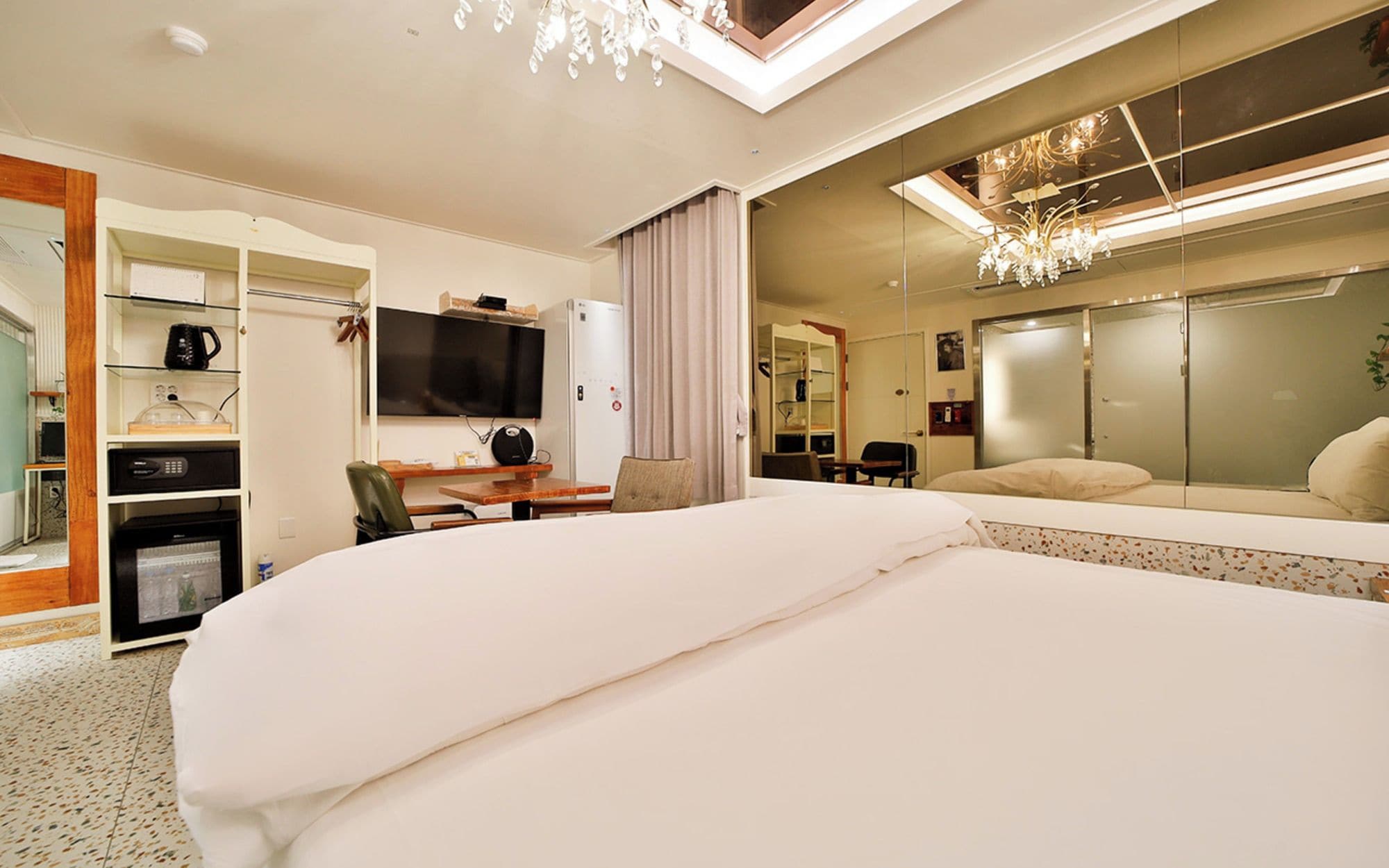 Habitación de hotel con una cama grande, un escritorio con silla, televisor, armario y espejo.