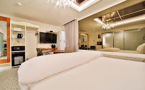 Habitación de hotel con una cama grande, un escritorio con silla, televisor, armario y espejo.