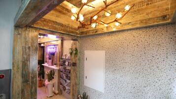 Un pasillo con techo de madera, una puerta blanca y una estantería llena de libros y plantas.