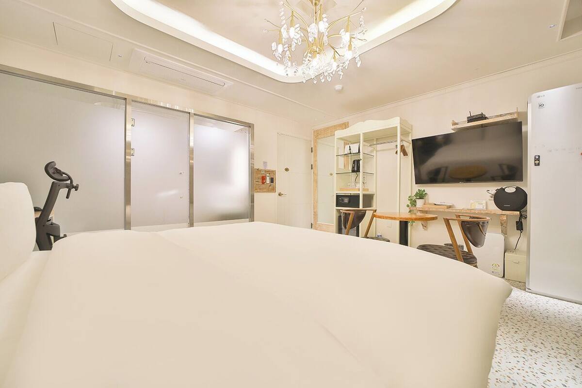 A modern hotel room with a large bed, a desk with a chair, a television, and a ceiling light fixture.