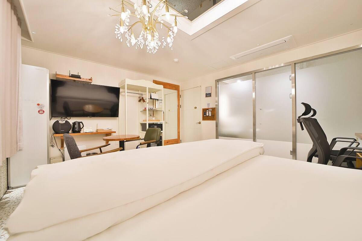 A modern hotel room with a large bed, a flat-screen TV, a dining area, and a sliding glass door.
