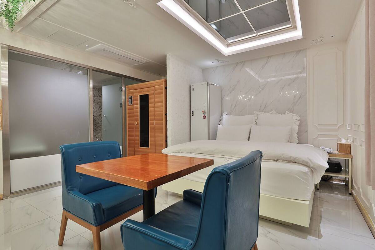 A modern bedroom with a large bed, a wooden table, and blue chairs.