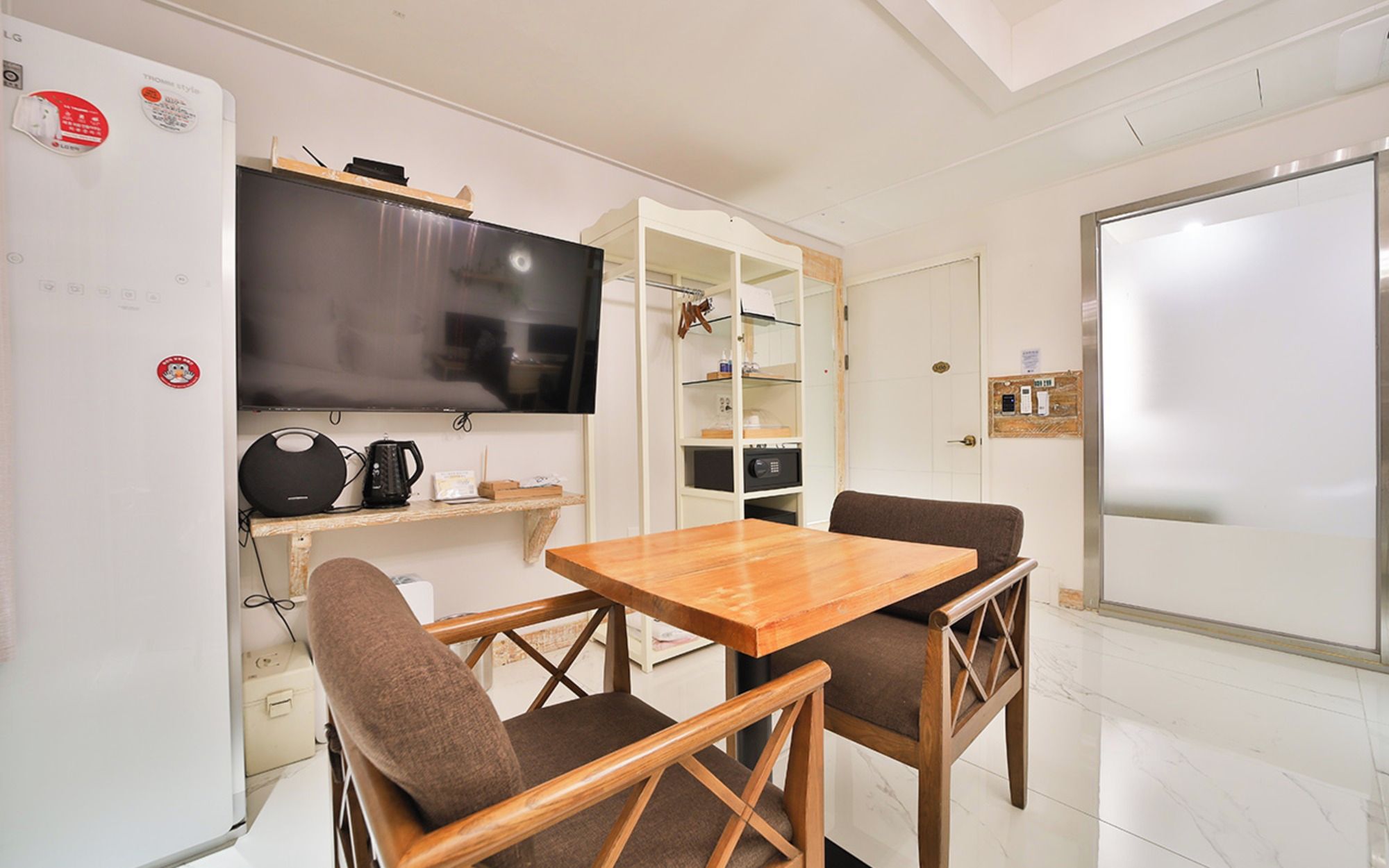 Un espacio habitable compacto con kitchenette, una mesa de comedor con dos sillas, un televisor de pantalla plana y una pizarra.