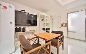 Un espacio habitable compacto con kitchenette, una mesa de comedor con dos sillas, un televisor de pantalla plana y una pizarra.