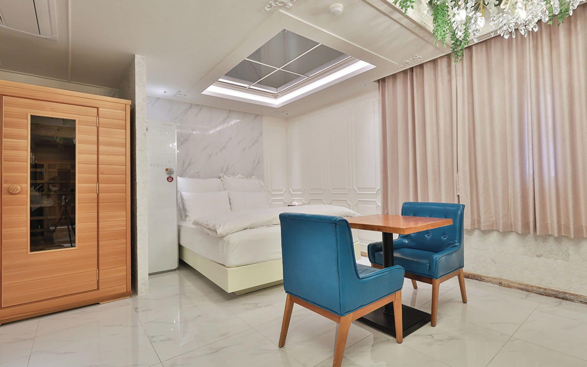 Una habitación con cama, un armario de madera, una mesa con dos sillas y una ventana con vista a un edificio.