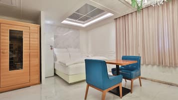 Una habitación con cama, un armario de madera, una mesa con dos sillas y una ventana con vista a un edificio.