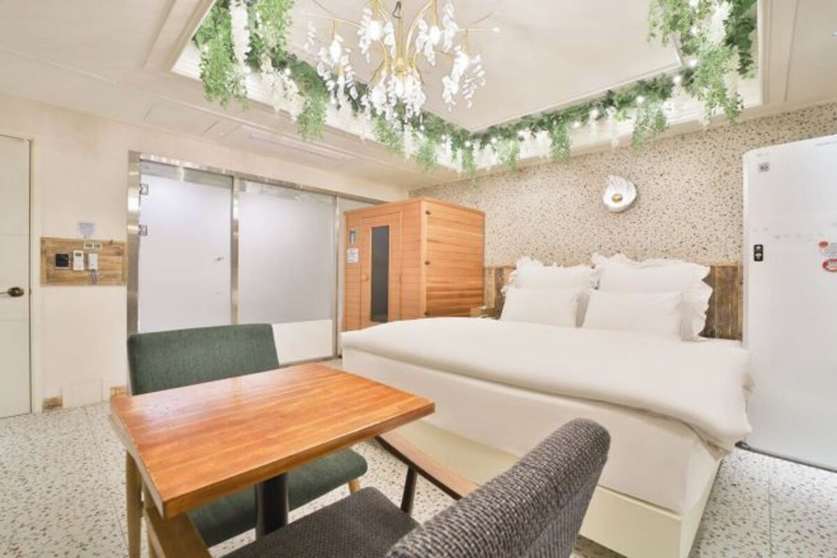 Una habitación con una cama, una mesa de madera, una silla, un armario pequeño y una lámpara fijada a la pared.