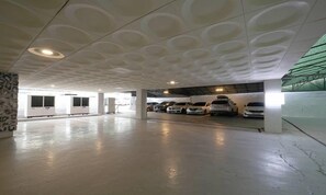 A parking garage with a modern ceiling design, several parked cars, and a clean, well-lit environment.