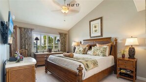 A bedroom with a wooden bed, two bedside tables with lamps, a window with curtains, a ceiling fan, and a framed picture on the wall.