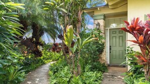 A tropical garden pathway leading to a building with a green door.
