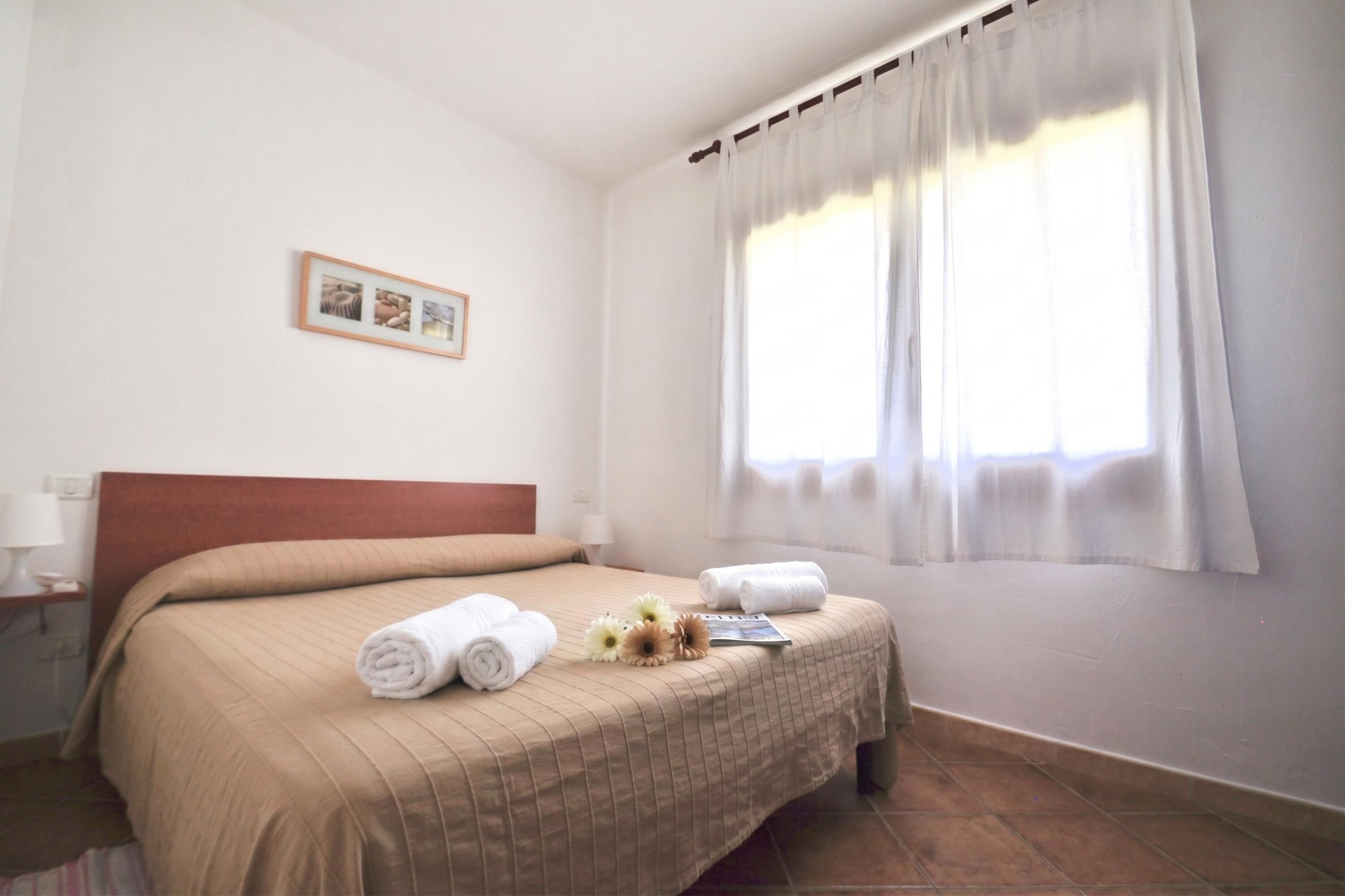 Una habitación de hotel con cama, mesita de noche, un cuadro en la pared y una ventana con cortinas.