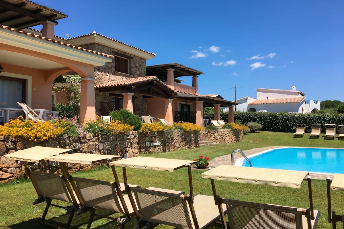 A poolside area with lounge chairs, a swimming pool, and a stone wall with flowers.
