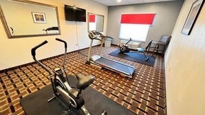 Ein Fitnessraum mit Trainingsgeräten, einem Fernseher und einem Fenster mit Jalousien.