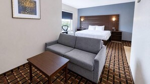Ein Hotelzimmer mit Bett, Sofa, Tisch, Stuhl und einem gerahmten Bild an der Wand.