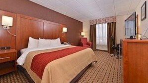 Une chambre d’hôtel avec un grand lit, une tête de lit en bois, un bureau avec une chaise, une lampe et un téléviseur.