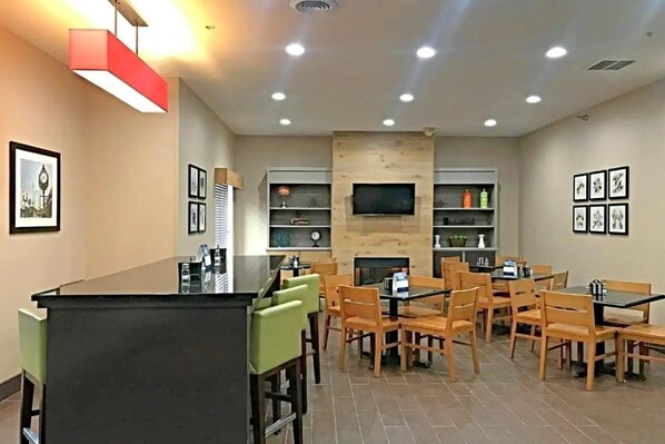 A modern dining area with a central island, wooden chairs, and a flat-screen TV mounted on the wall. - Comfort Inn & Suites Ofallon - St Louis Area (O'Fallon)
