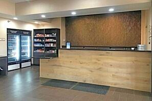 A reception area with a wooden reception desk, a refrigerator stocked with beverages and snacks, and a wall-mounted display. - Comfort Inn & Suites Ofallon - St Louis Area (O'Fallon)