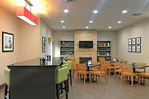 A modern dining area with a central island, wooden chairs, and a flat-screen TV mounted on the wall. - Comfort Inn & Suites Ofallon - St Louis Area (O'Fallon)