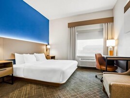 Una habitación de hotel con una cama grande, un escritorio, una silla y un ventanal con cortinas.