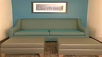A room with a teal sofa, two matching ottomans, a patterned carpet, and a framed picture on the wall.