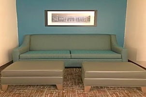 A room with a teal sofa, two matching ottomans, a patterned carpet, and a framed picture on the wall.