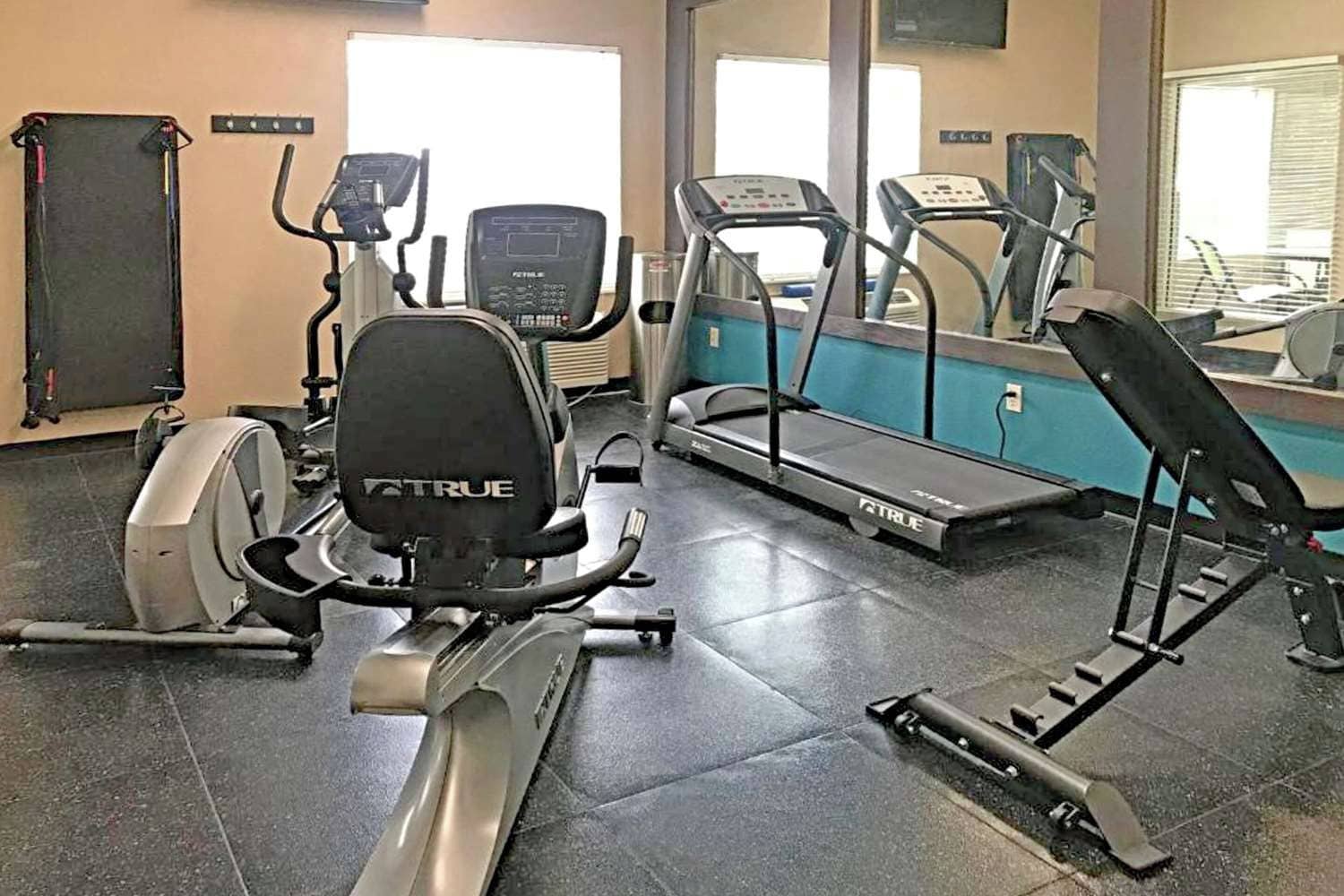 A gym with various exercise equipment including a stationary bike, elliptical, treadmill, and weight bench.