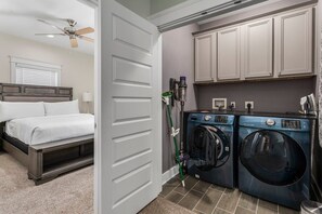 Un dormitorio con cama, ventilador de techo y un área de lavandería con dos lavadoras.