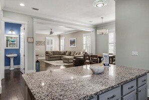 A modern kitchen with granite countertops, a dining area with a table and chairs, and a living room with a sofa and a ceiling fan.