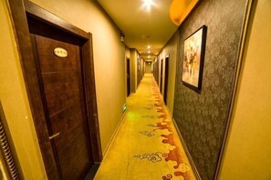 Un pasillo de hotel con puertas de madera, alfombra estampada y cuadros en las paredes.