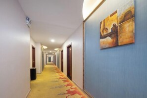 A hotel hallway with a carpeted floor, doors on both sides, and a painting on the wall. - Moore Hotel Yuxi (Yuxi)