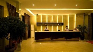 Zona de recepción con una larga mesa, dos recepcionistas y plantas en macetas.