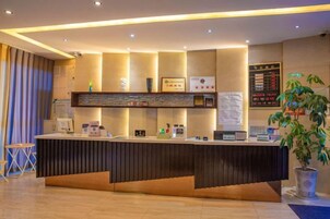 A reception desk with a modern design, a potted plant, and a wall-mounted information board.