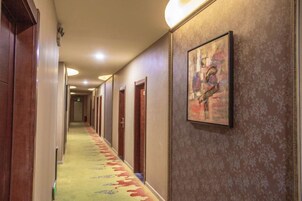 Pasillo de hotel con puertas a ambos lados, alfombra estampada y un cuadro en la pared.