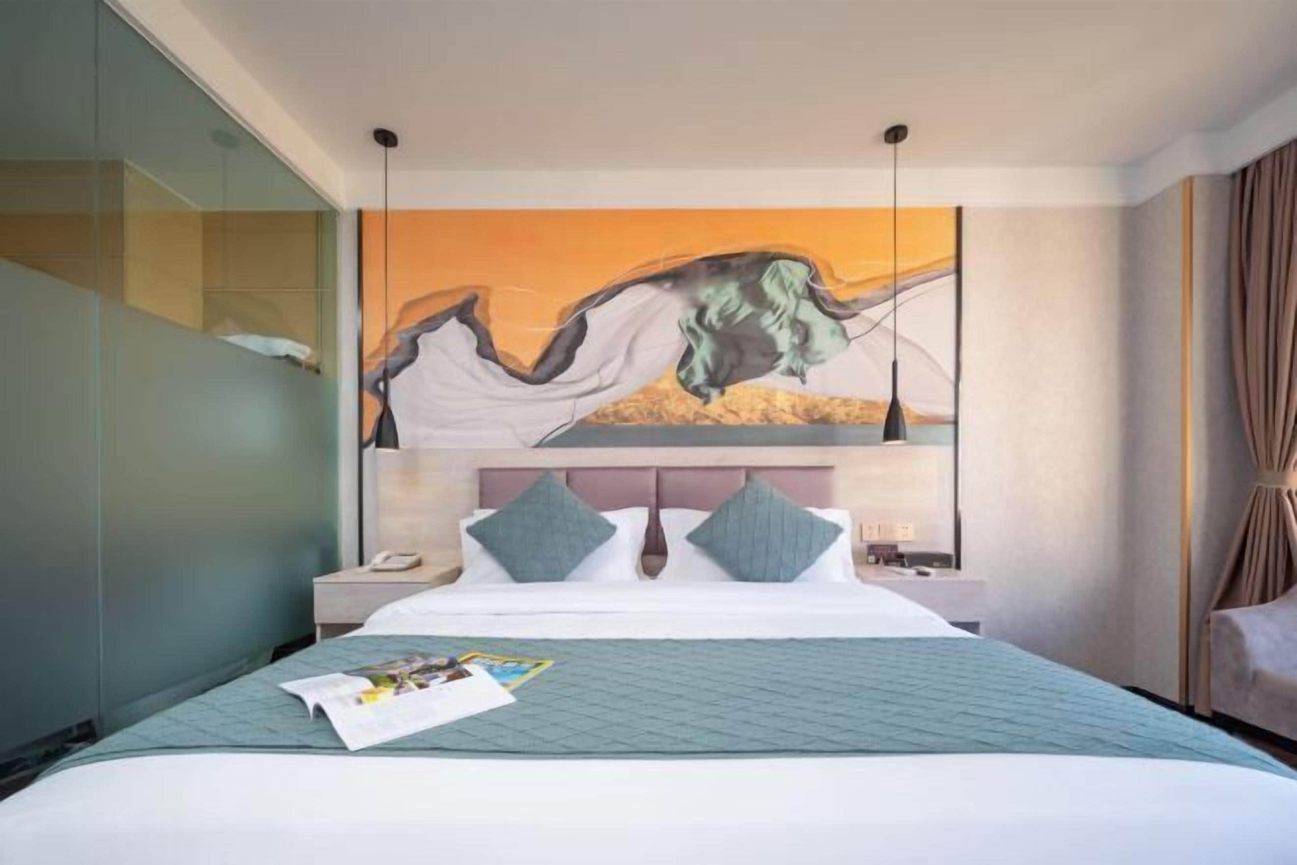 A modern hotel room with a large bed, a nightstand, a wall-mounted painting, and a glass partition.